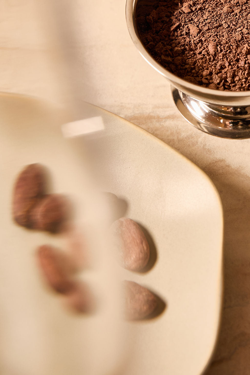 Close-up of raw cacao beans and cacao powder in a bowl on a marble countertop.