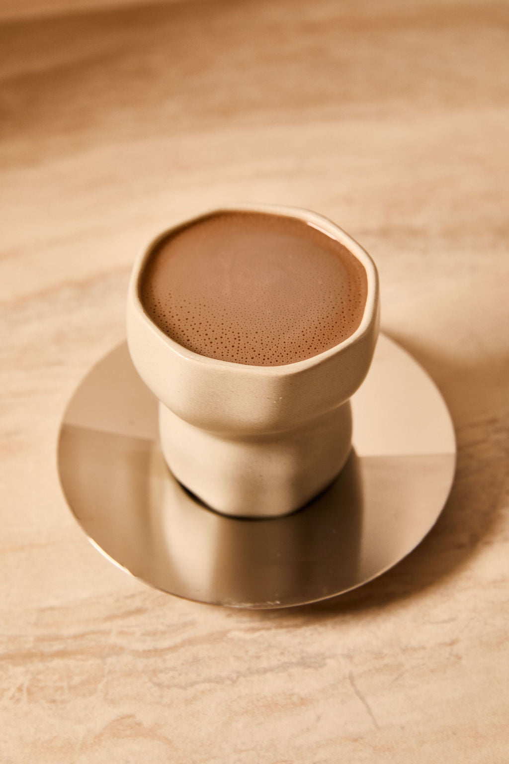 Minimalist beige ceramic cup filled with ceremonial cacao placed on a round brass coaster.